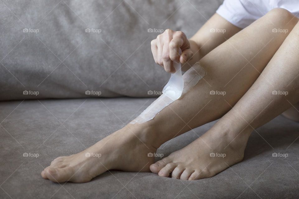 Faceless girl removing hair from legs with depilation cream 