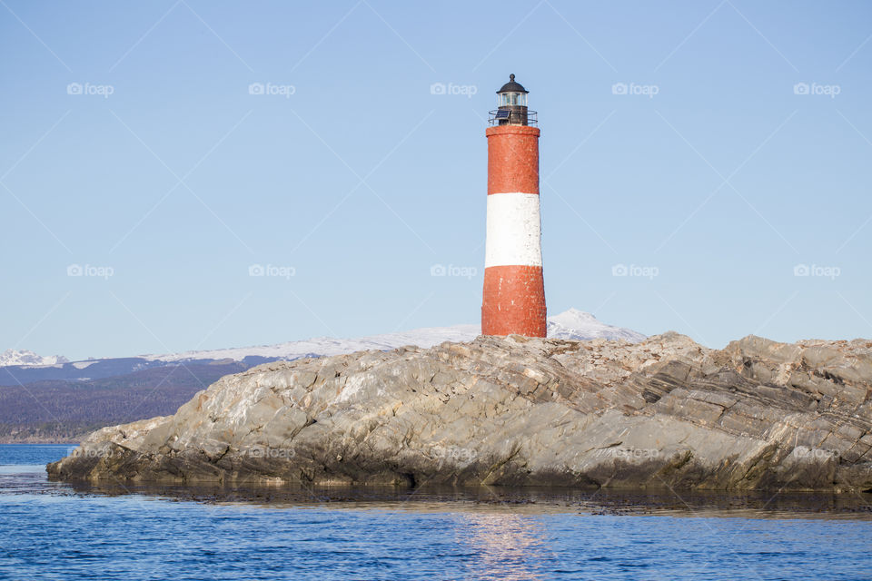 lighthouse on an island with snowy mountains at the back