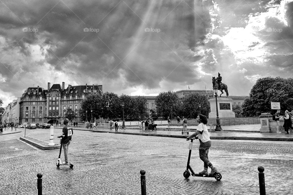 teenagers ride scooters in the sunshine in the center of Paris