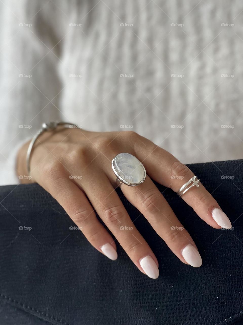 Woman's hand wear white nail polish and silver bracelet and ring adorned with moonstone, grabs a black clutch bag