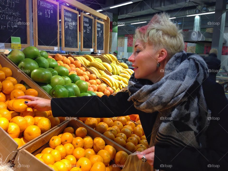 Young wooman with white-pink hairs choosing mandarins from the row of fruits in the marketplace