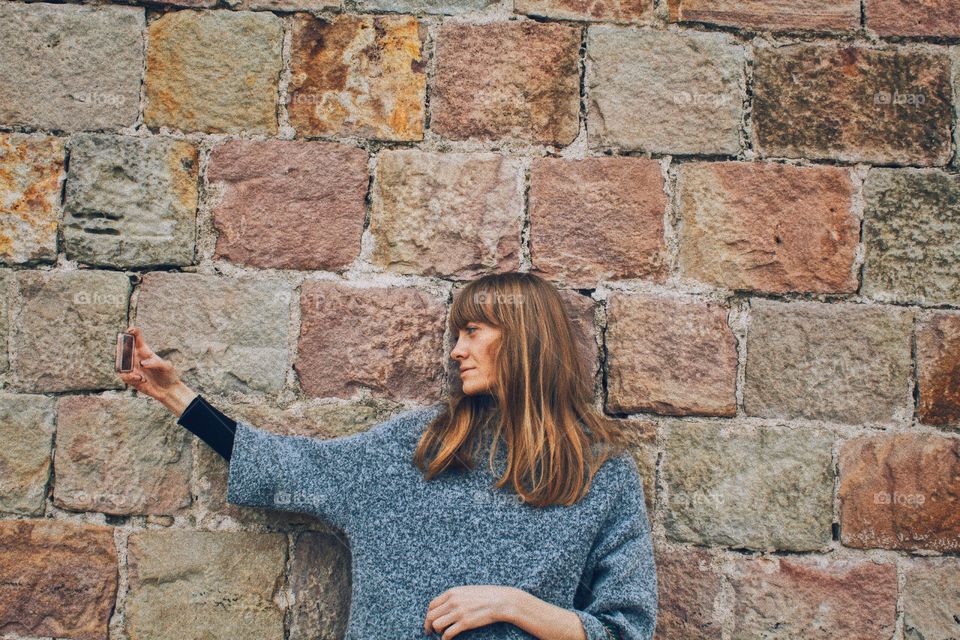 Woman taking selfie with smartphone against stone wall