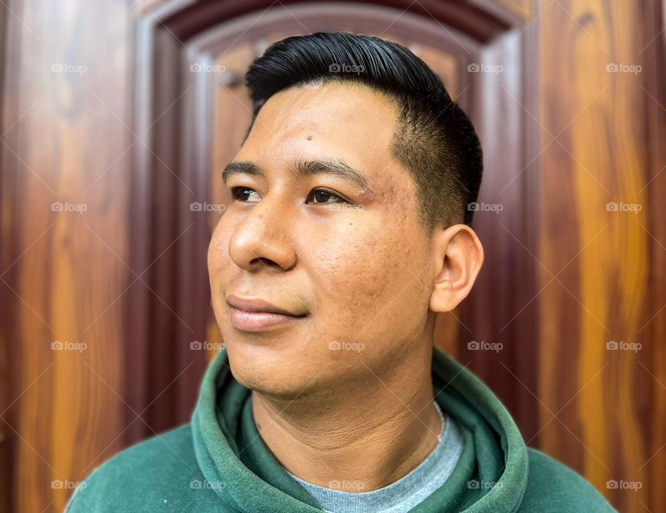 dark-skinned man, with pimples and pimple scars, wearing a green sweater and wooden door background