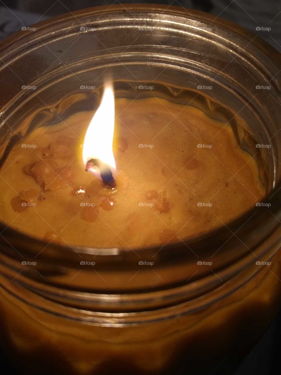 Newly lit orange, butterscotch candle in a mason jar with the reflection from the flame highlighting the edge of the glass.