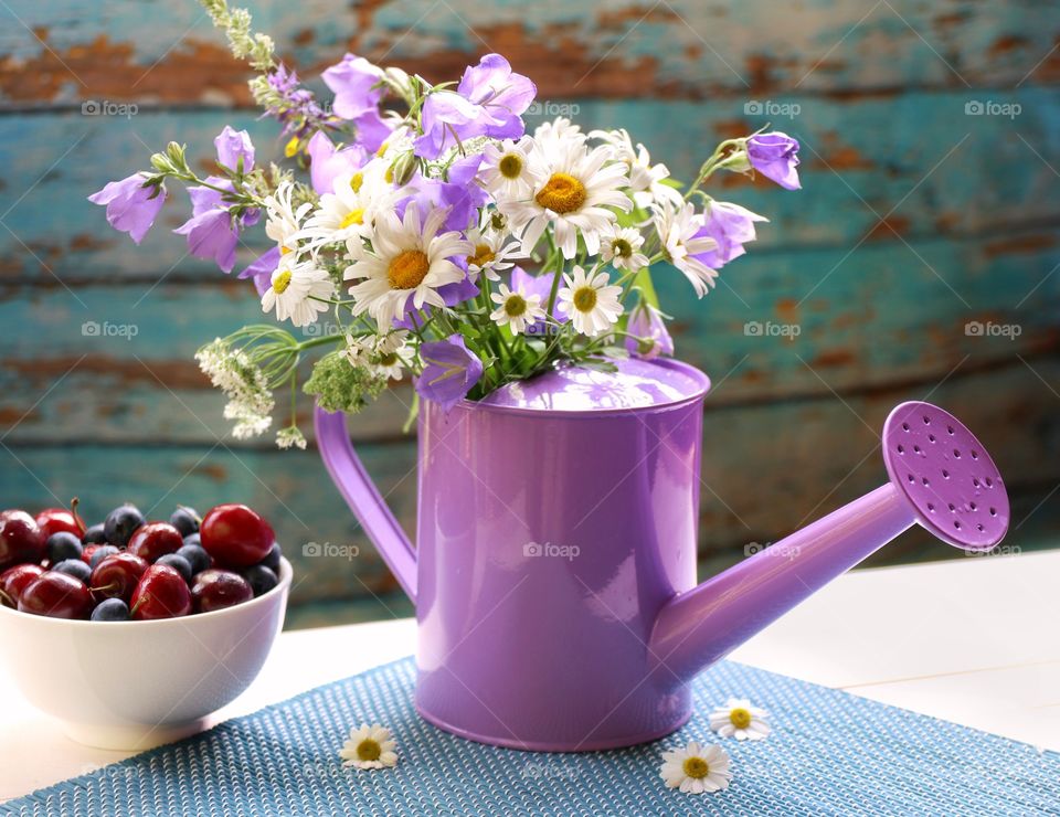 summer wild flowers in a purple watering can and fresh berries 