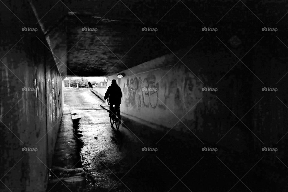 black and white picture from a small tunnel with a cyclist cycling to the light at the end of the tunnel