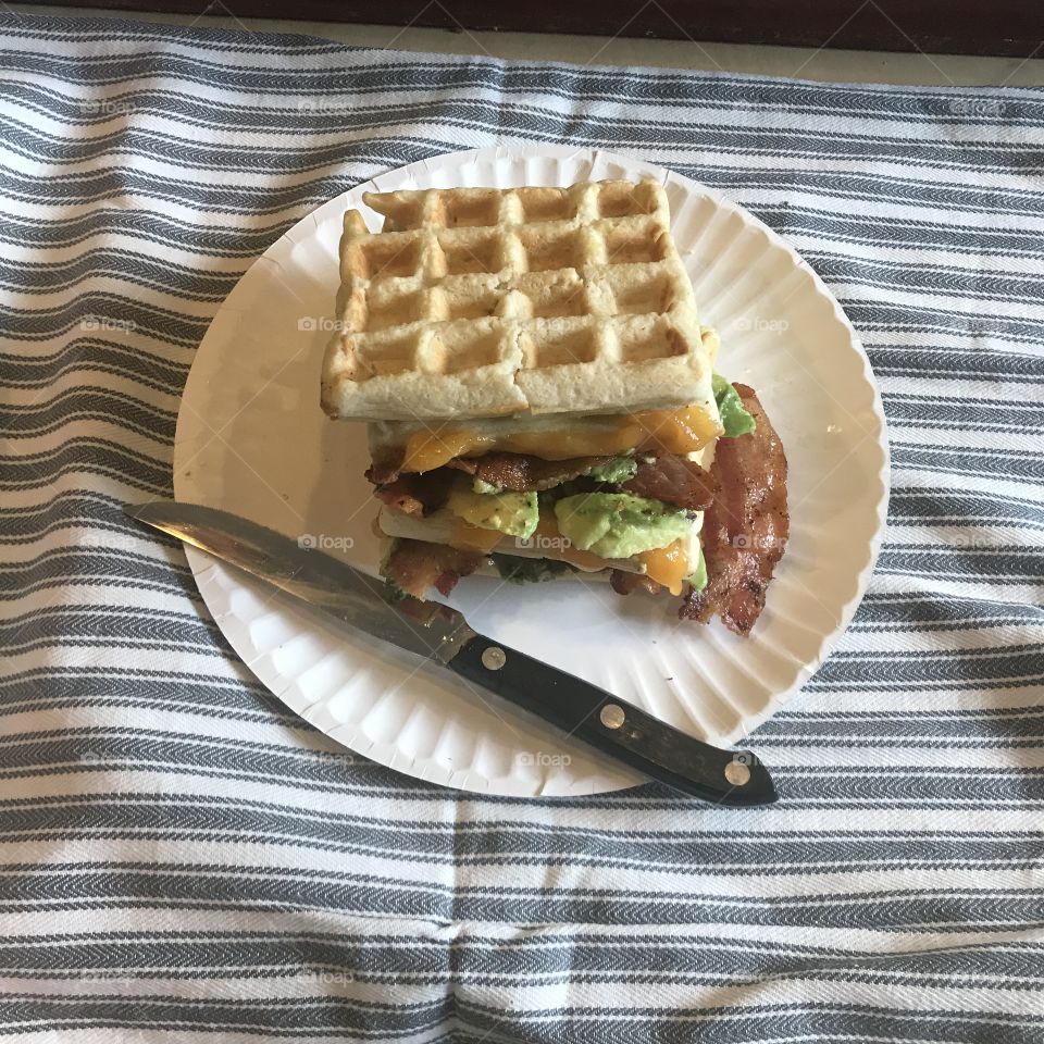 A healthy waffle avocado, cheese and bacon sandwich on a white plate displayed on a blue and white cloth. USA, America 