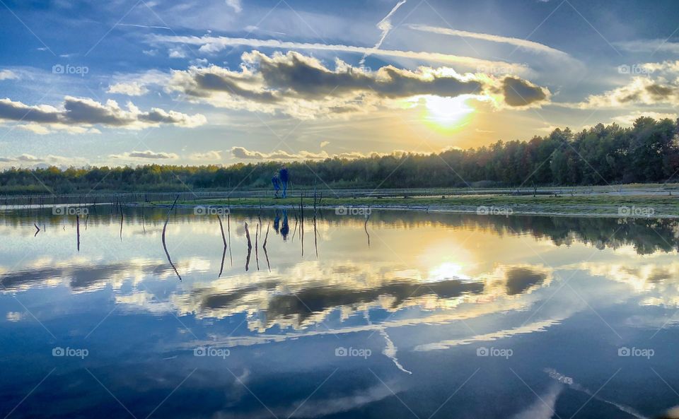 Dramatic sunset sky and two silhouettes walking in nature reflected in the water of a forest lake