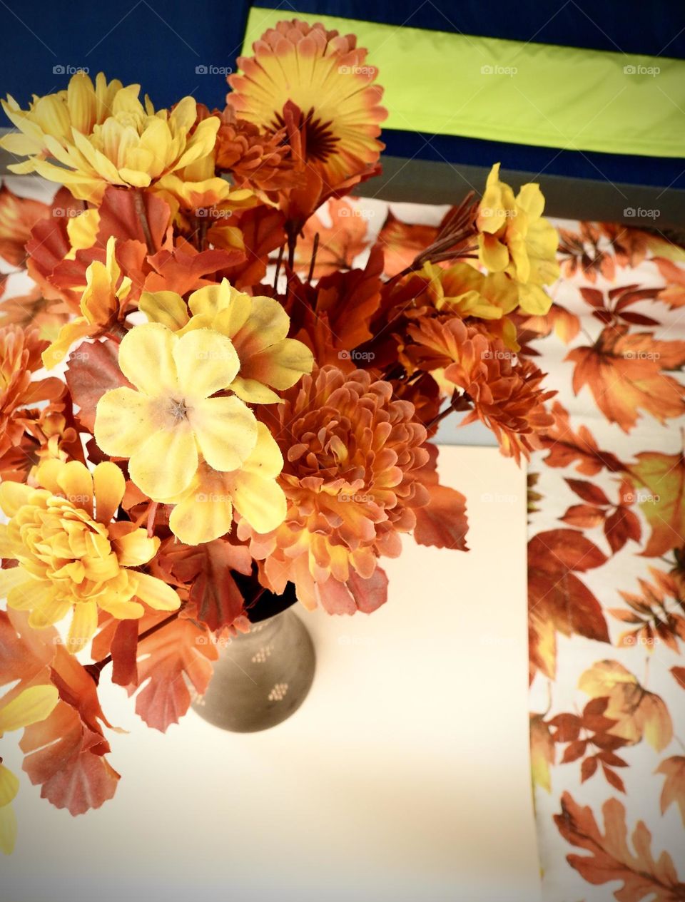 Orange yellow bouquet representing fall autumn on top of a beige background and cloth with orange leaves drawing with a blue and green tent during camping.