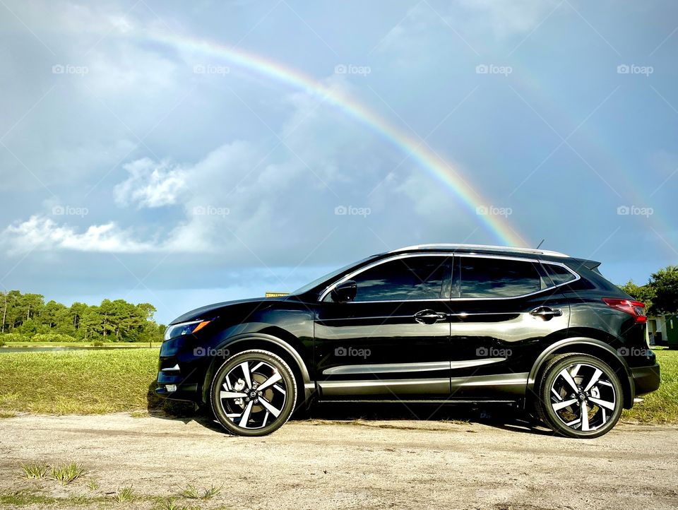 Shiny new Black suv crossover Nissan car parked on dirt road with a rainbow in the sky 