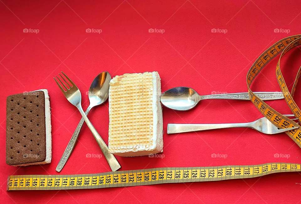 Rectangles.On a red background lies of ice cream with chocolate waffles and of ice cream with white waffles.Between the ice cream lie a crossed fork and spoon.Behind the white ice cream lie a fork and a spoon in the shape of an inverse proportional