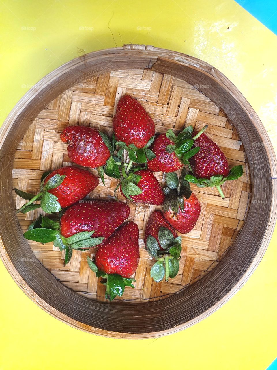 red and fresh strawberries are placed on a rattan plate  on a yellow table at home