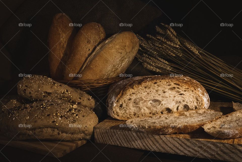 A selection of bread and rolls with wheat under a low warm light, against a sackcloth backdrop 