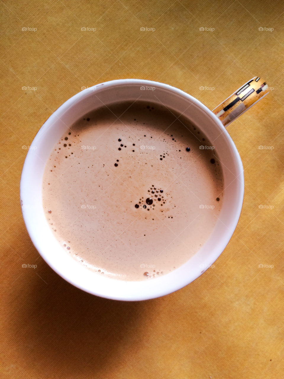 Coffee with foam in a cup on a yellow tablecloth