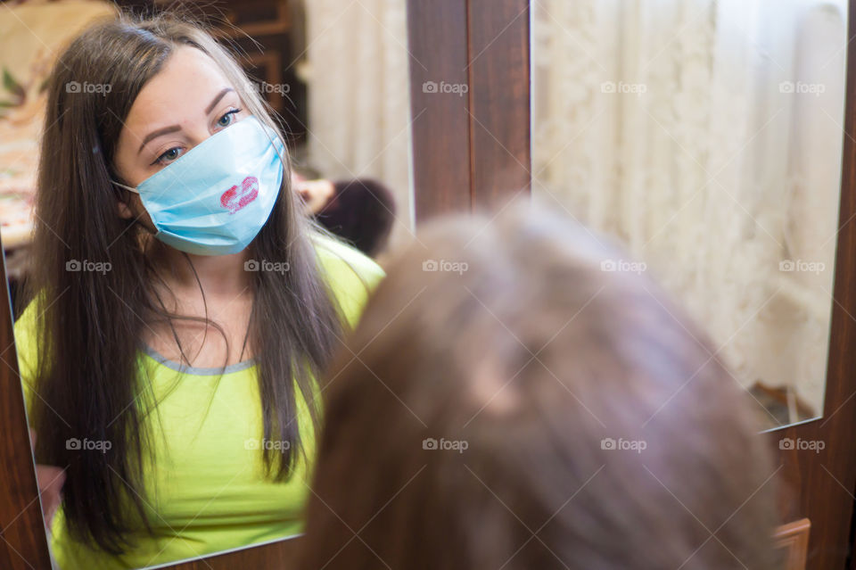 A young girl does makeup for a walk outside in a protective mask against the coronavirus pandemic, her lips are painted with red lipstick.