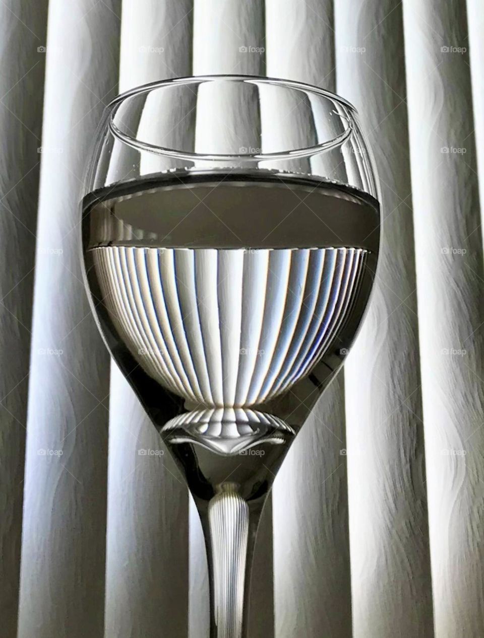 Wine glass half full of water catching the reflection of the dining room blinds 