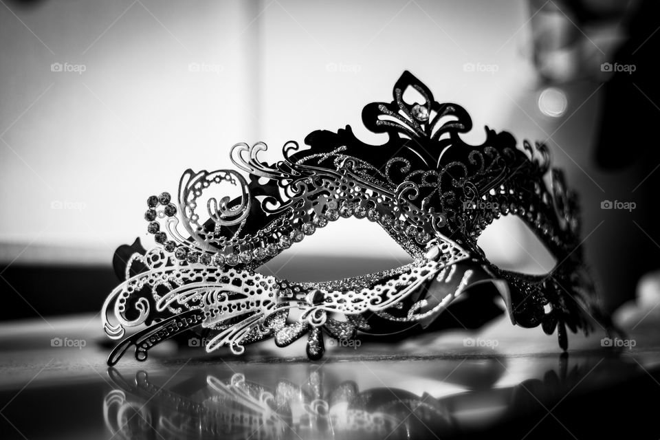 A black and white portrait of a venetian mask full of mystery and excitement in front of a window on a windowsill.
