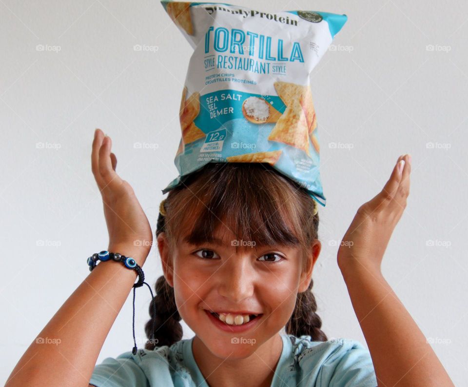 Cute happy girl balancing bag of chips on her head