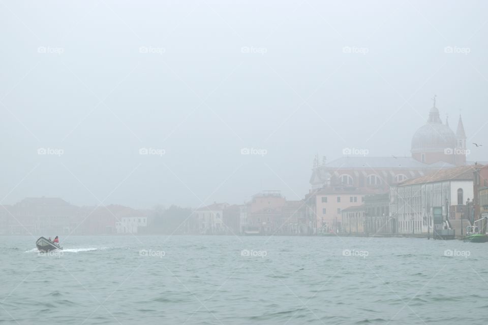 Venice on a foggy day with ond boat in the foreground.