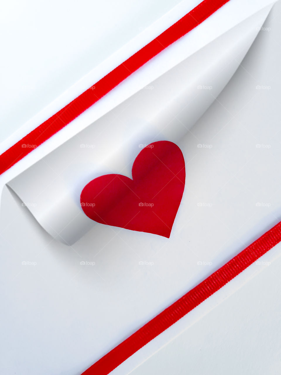 Flat lay concept photo: Turning the page on love. A white background with two red straight line ribbons and a red heart between.