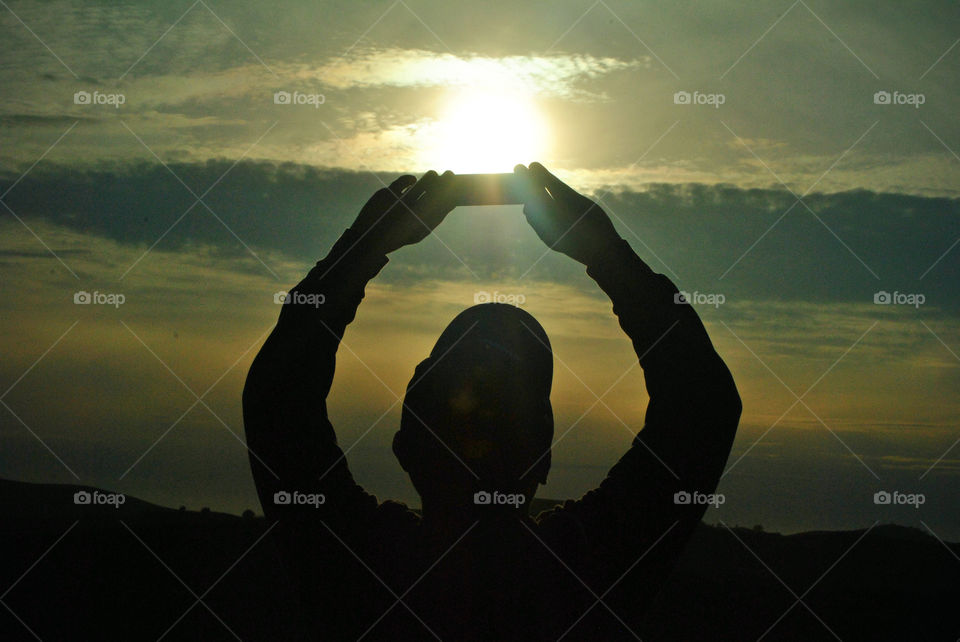 man taking a photo using mobile phone during sunset