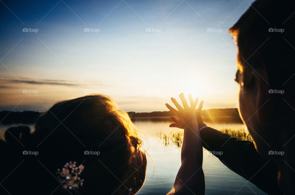 Happy adult woman and man holding hands against the sun at sunset. Silhouette of the couple