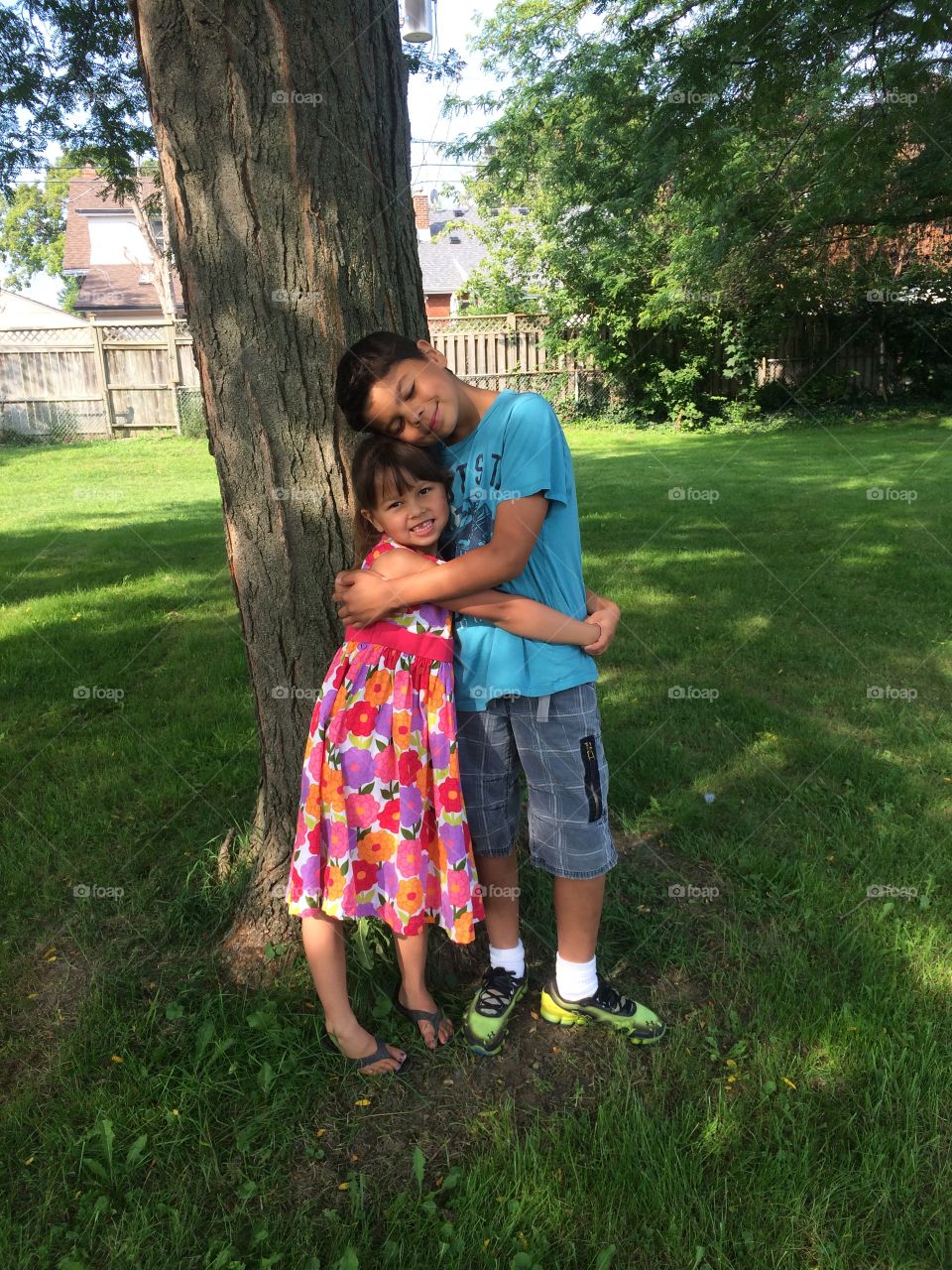 Happy brother and sister standing under tree trunk