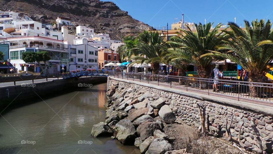 Puerto de Morgan
Gran Canaria
Puerto de Mogán is a picturesque resort and fishing village in the municipality of Mogán, set at the mouth of a steep-sided valley on the southwest coast of the island of Gran Canaria. It attracts many tourists either to stay or on day-visits. Canals linking the marina to the fishing harbour have led to it being nicknamed "Little Venice" or the "Venice of the Canaries". Restaurants and bars fringe the marina and the beach front. On Fridays there is a very popular market which brings in tourists from all over the island.
Puerto de Mogán has very few buildings over two stories high, and the government of Gran Canaria restricts new buildings taller than this.
Puerto de Mogán can be reached via a new extension of the motorway GC1 (opened in March 2013) which