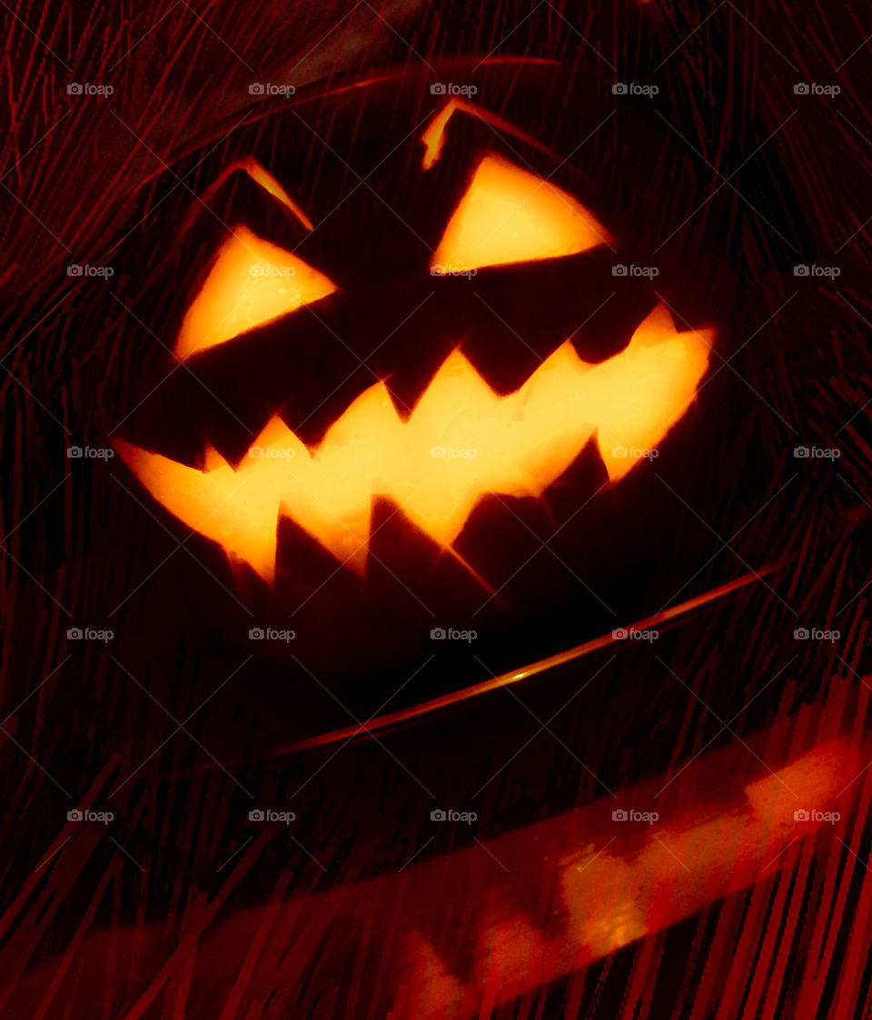 A pumpkin carved with a menacing grin, lit up by orange candle light and surrounded by a red lined pattern