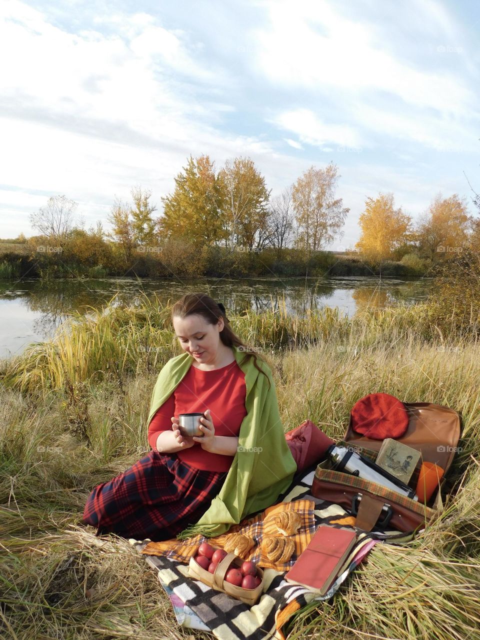 Autumn picnic - a girl enjoys hot tea on the banks of the river
