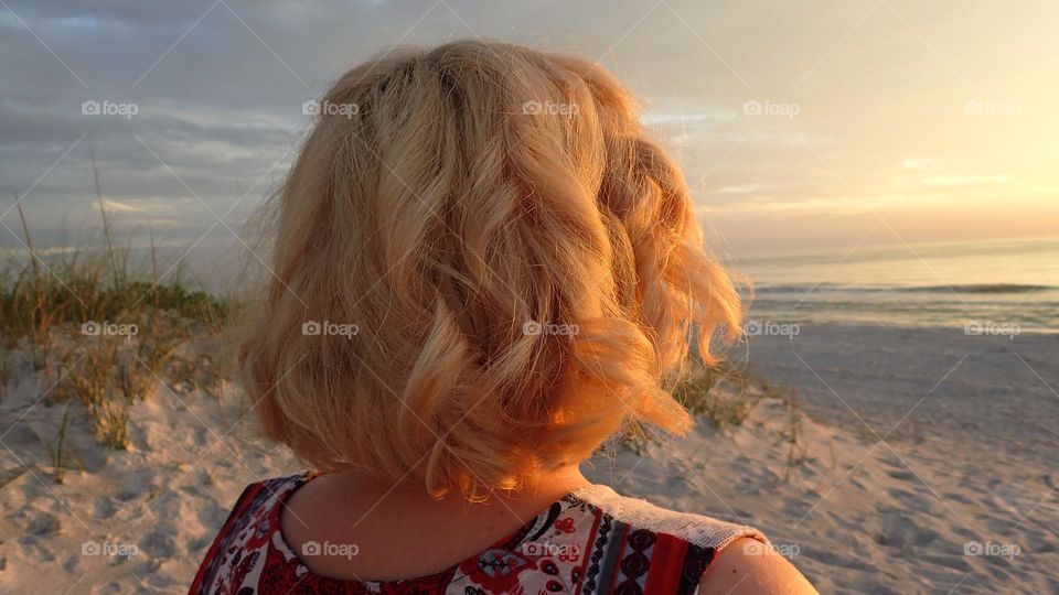 Shoulder length curly blonde hair full of body luscious healthy woman watching sunset at beach