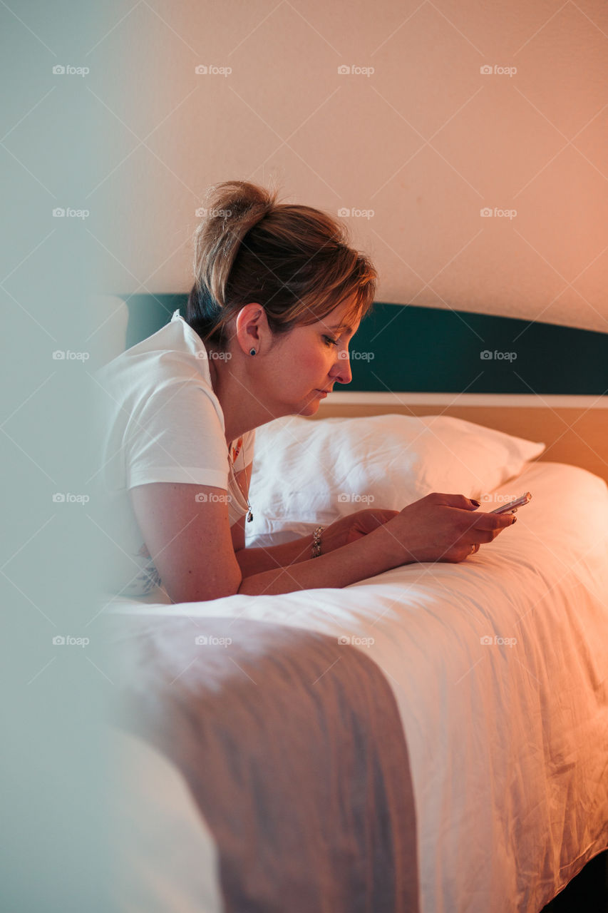 Young woman using smartphone while laying in bed in bedroom