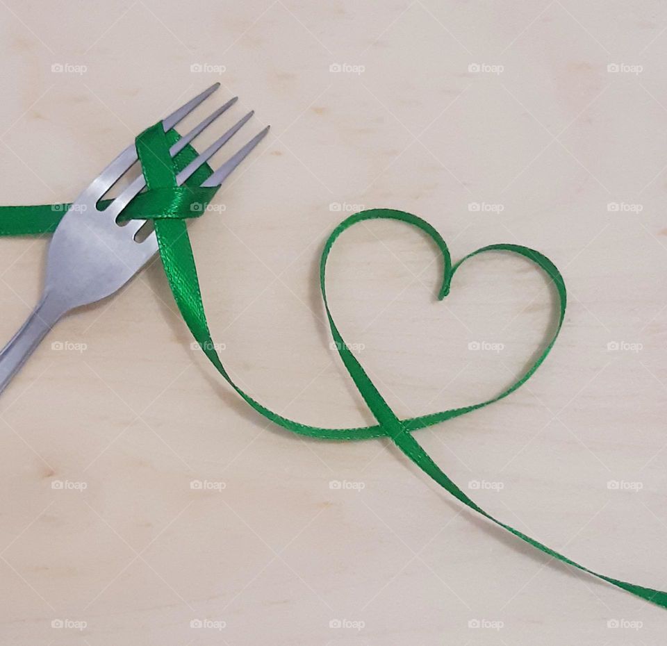 Fork and ribbon with shape heart isolated on wooden background. Beautiful green colour of ribbon