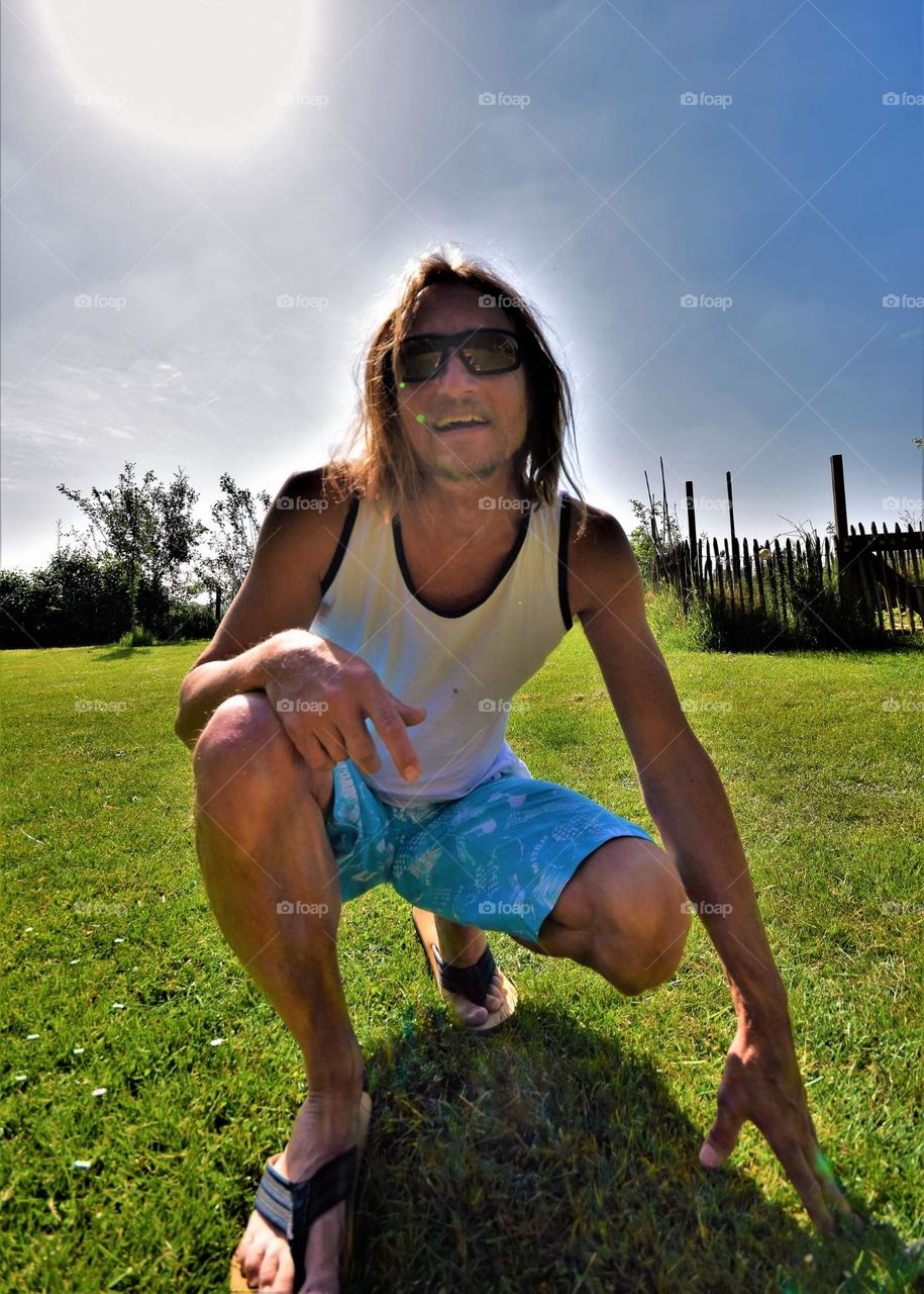 happy and energetic man with sunglasses posing on green grass on a warm summers day wide angle frog perspective portrait