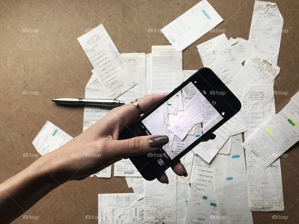 Female hand holding a mobile phone and taking a photo of bills on wooden table for planning budget 