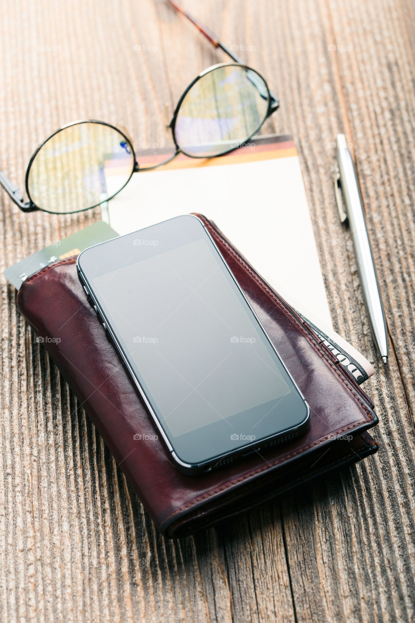 Smartphone with blank screen, wallet, dollar banknotes, debit credit cards and notebook on wooden table. View from above. Portrait orientation