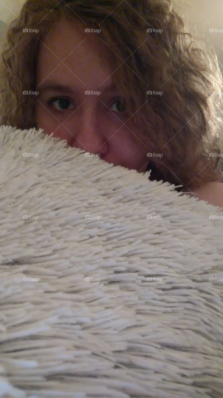 a frizzy haired girl peaking out from behind a fuzzy blanket