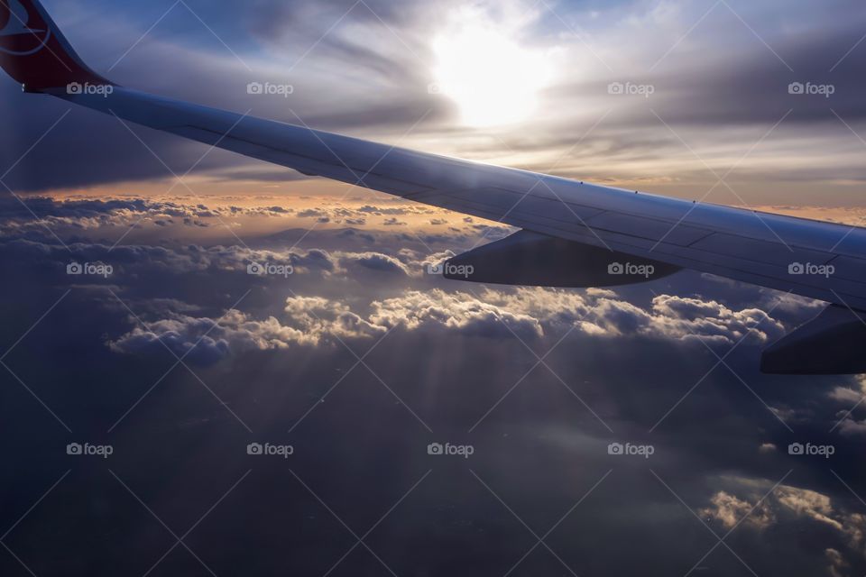 Airplane wing above the clouds with sunbeams
