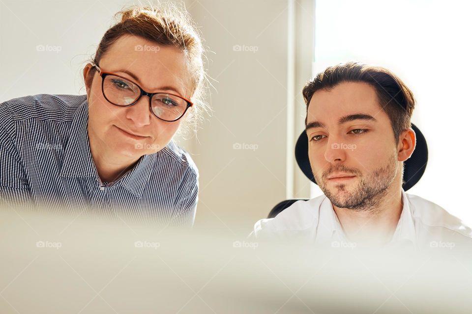 Two business people discussing financial data looking at computer screen. Businesswoman talking to young male coworker in office. People entrepreneurs having conversation working together. Workmates talking about project