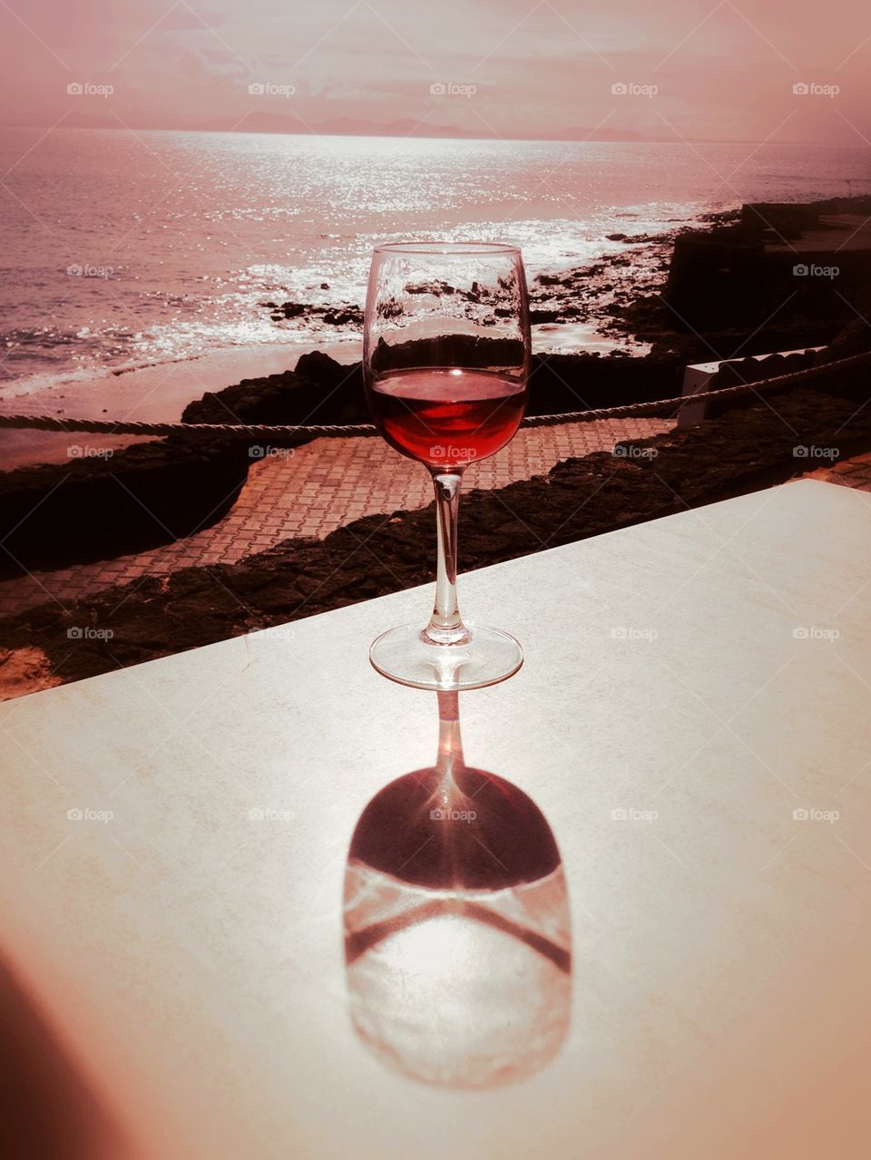 Reflection of red wine glass on table near the beach