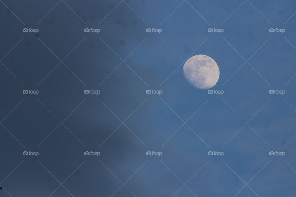 Closeup of waxing gibbous spring moon in blue sky half filled with dark misty clouds 