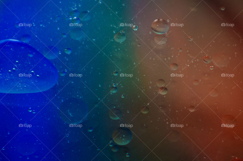 Bubbles of vegetable oil in clear water on a glass and transparent lid from a frying pan on colored paper.