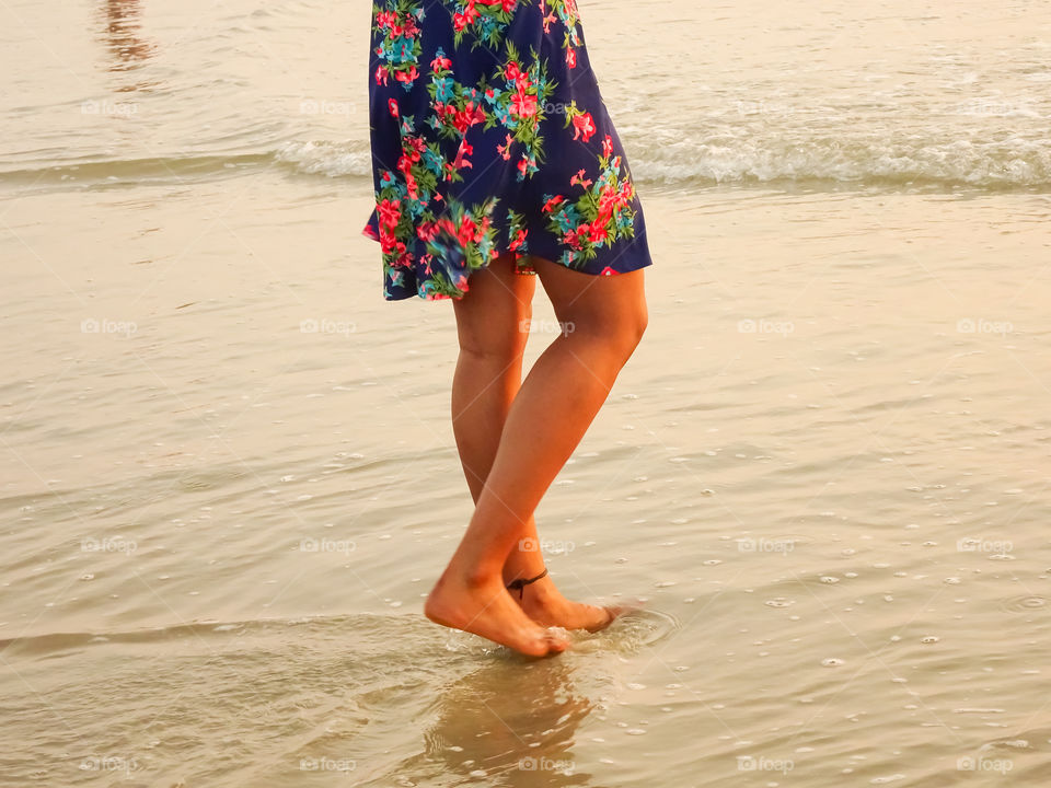 young woman standing with bare feet on the wet sand of the sea during golden hours