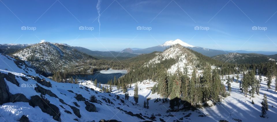Snowy mountain top looking out into the lakes and mountains in the distance covered by trees 