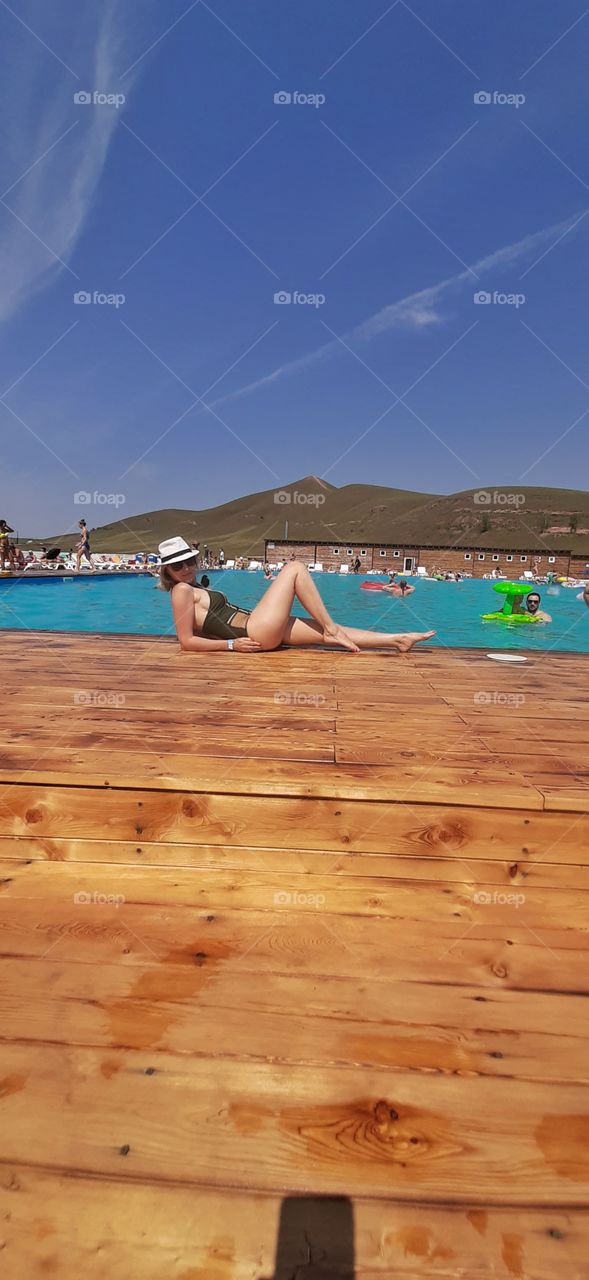 девушка в шляпе и закрытом купальнике сидит около бассейна