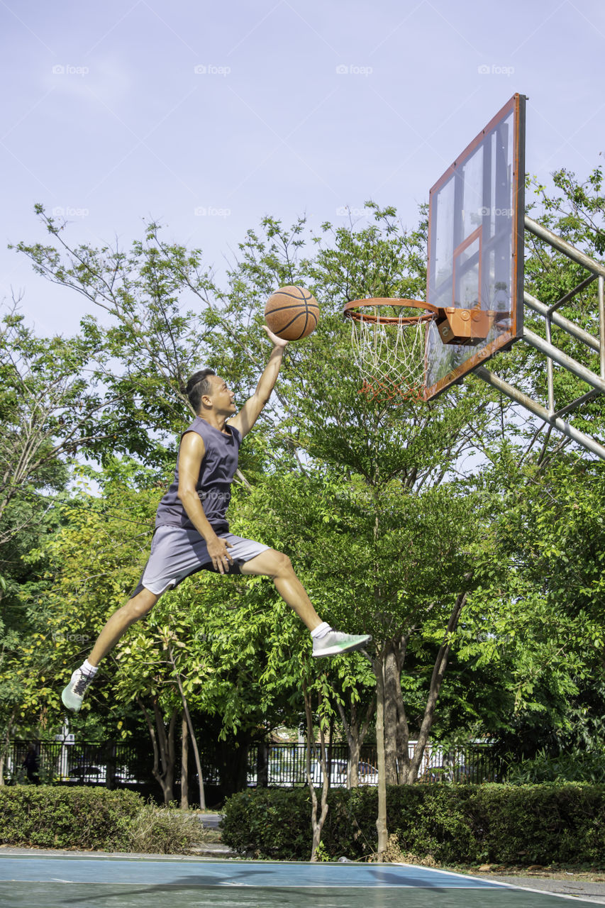 Basketball in hand man jumping Throw a basketball hoop Background  tree in park.