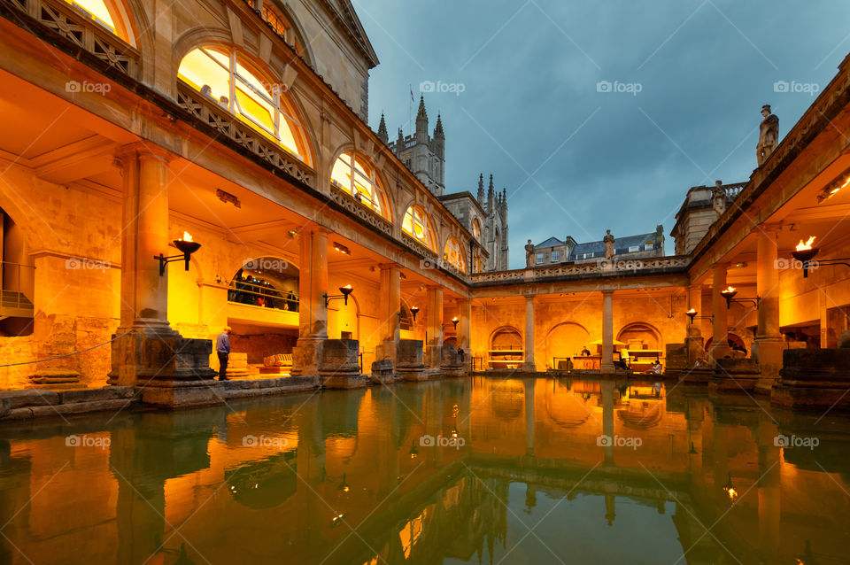 Evening sconces light scenery of the courtyard in restored ancient Roman Baths by the main spa pool.  City of Bath. UK.