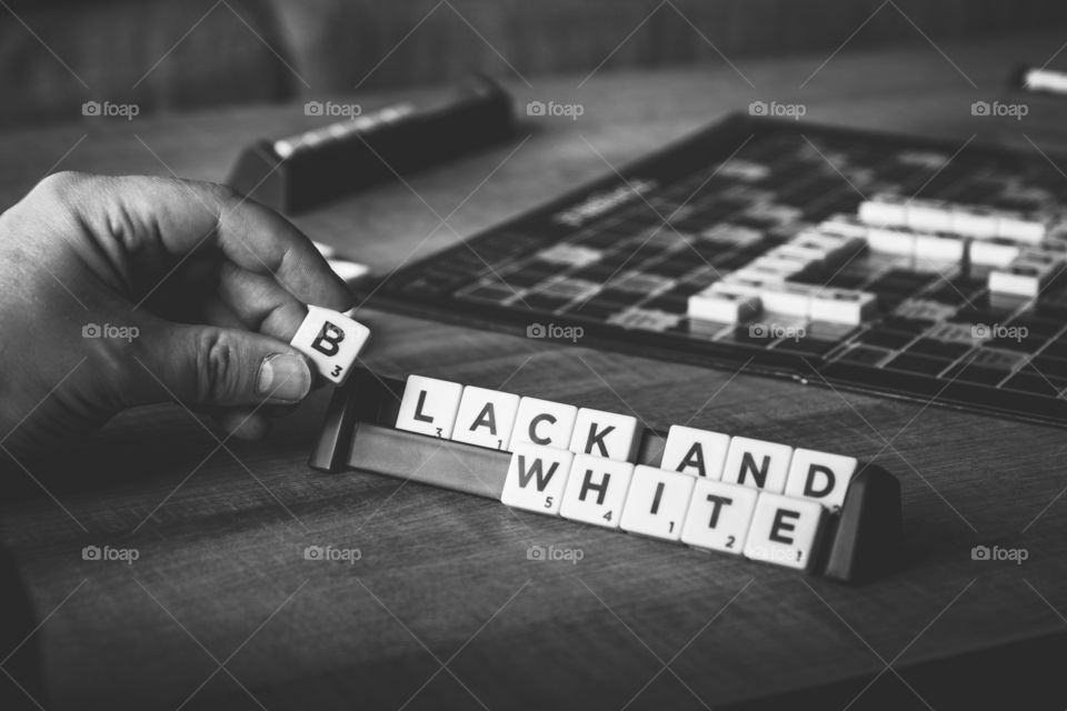 A black and white portrait of a scrabble board of a player almost spelling black and white. the last letter is in his hand.