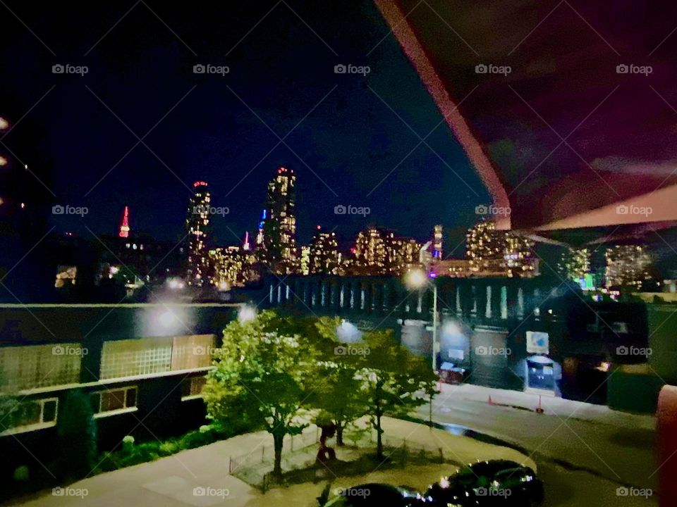 This nighttime panoramic view from the pedestrian lane of the „Pulaski Bridge“ at „Newtown Creek“ shows the skyline of LIC, Queens and partially further back also of „Manhattan“ in particular the „Empire State Building“. 2022. Hypnotic Productions