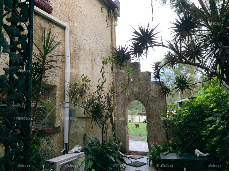 White and red spanish old style architecture residential large house built in the early 1900s. Other entrance opening with antique style door, view on both side of the wall, looking up to the steps stairs style wall with trees, and vegetation growth.